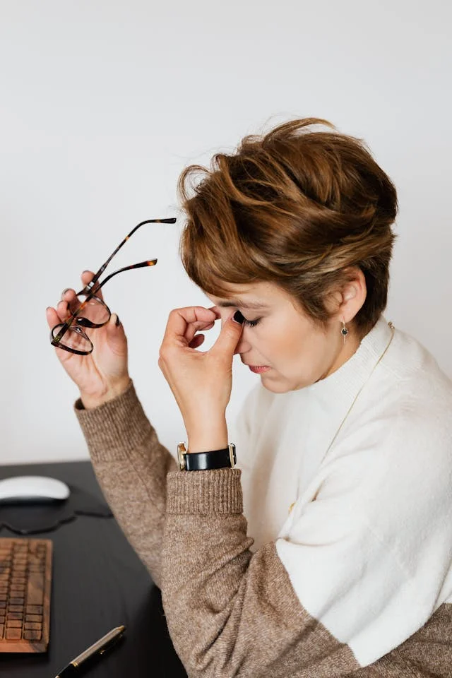 A caregiver at her desk, glasses off, eyes closed in exhaustion